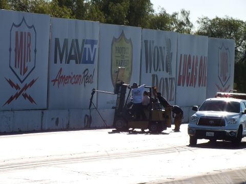 2003 Ford Crown Victoria - Crew members ride a yellow forklift handling track equipment beside a Lucas Oil and MAVTV banner wall, with a white truck nearby.