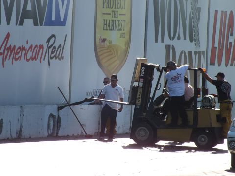 2003 Ford Crown Victoria - Track crew handle a long pole near a yellow Yale forklift in front of sponsor banners at a drag strip.
