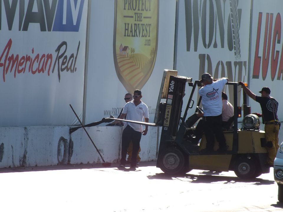 Workers with a long pole and a yellow forklift by a banner wall