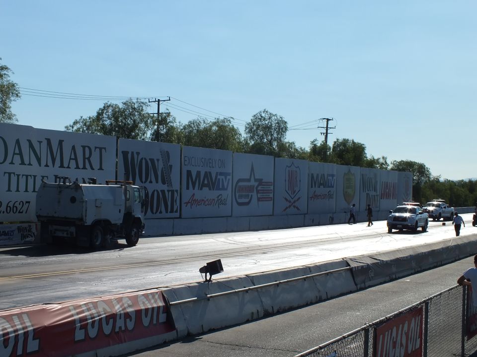 Track-drying truck and white trucks on a drag strip beside banner wall
