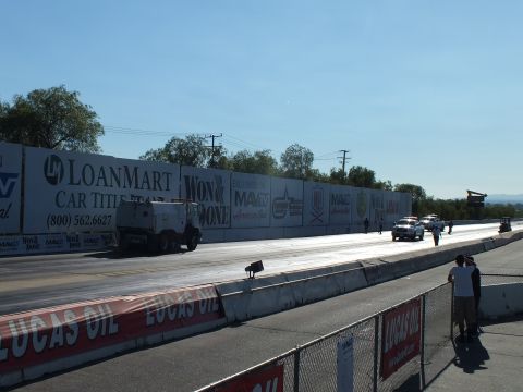 2003 Ford Crown Victoria - white service truck moves down the drag strip past a LoanMart Car Title banner with spectators watching from the rail.