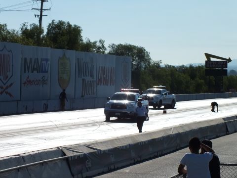 2003 Ford Crown Victoria - White trucks line up at the drag strip start as a track official stands on the surface and spectators watch behind the fence.