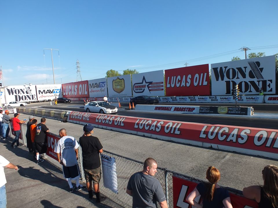 Drag strip lanes with cars staging and spectators along the fence