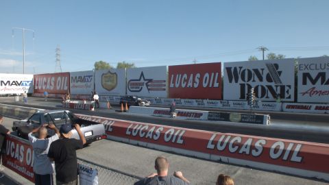 2003 Ford Crown Victoria - Spectators crowd the fence as a dark car stages at the drag strip start line under Lucas Oil and Won & Done banners.