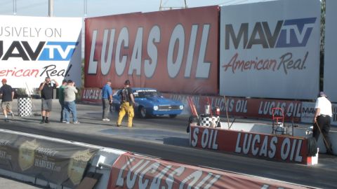 2003 Ford Crown Victoria - blue muscle car performs a burnout at the start line as crew and photographers stand by Lucas Oil and MAVTV banners.