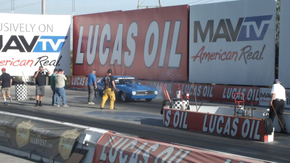 Blue muscle car doing a burnout with crew at the drag strip start