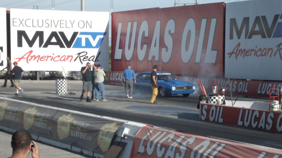 Blue muscle car smoking its tires at the drag strip with onlookers
