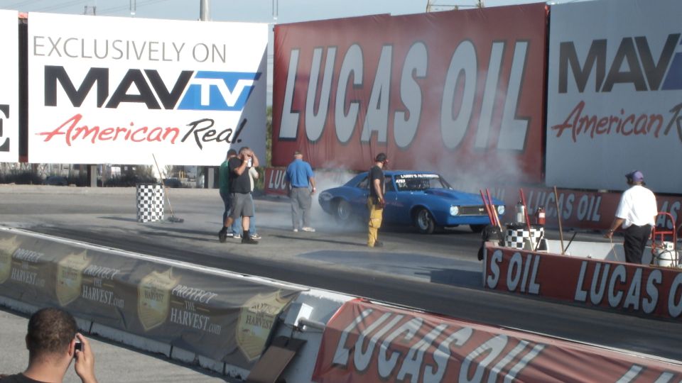 Blue muscle car in tire smoke at the drag strip start with crew nearby