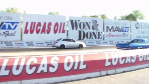 2003 Ford Crown Victoria - white sedan and a blue car line up on a drag strip flanked by Lucas Oil and Won & Done banners.