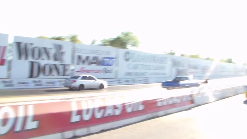 Silver car and blue car racing down a drag strip in bright sunlight