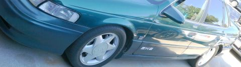 1993 Ford Taurus - A green 1993 Ford Taurus is viewed from the front quarter, highlighting its distinctive body style and wheel design.