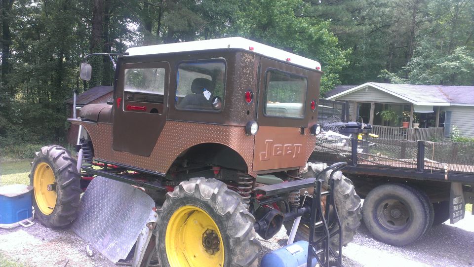 Brown Jeep with large tractor tires and a white roof, seen from the rear quarter