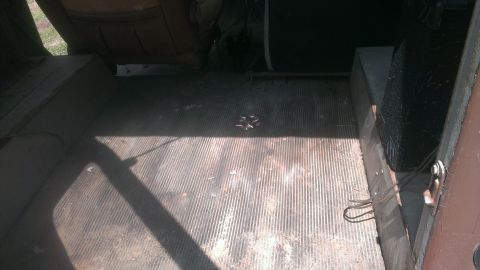1978 Ford Bronco - The interior cargo area of a vehicle shows a ribbed floor mat and the well for a spare tire.