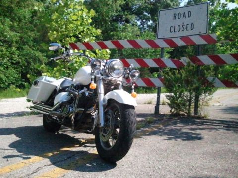 1995 Ford F-150 - A white motorcycle is stopped at a road closure barrier, with a 'ROAD CLOSED' sign overhead.