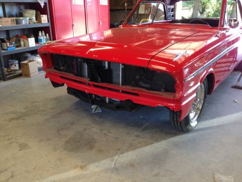 1964 Ford Fairlane - The front of a red 1964 Ford Fairlane is visible, missing its bumper and grille, in a garage setting.