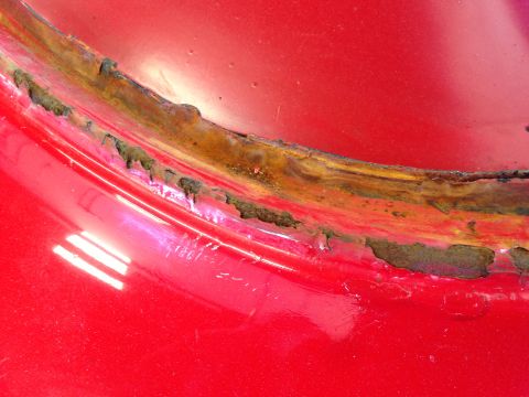 1964 Ford Fairlane - The red paint is peeling away to reveal significant rust on this vehicle's body panel.
