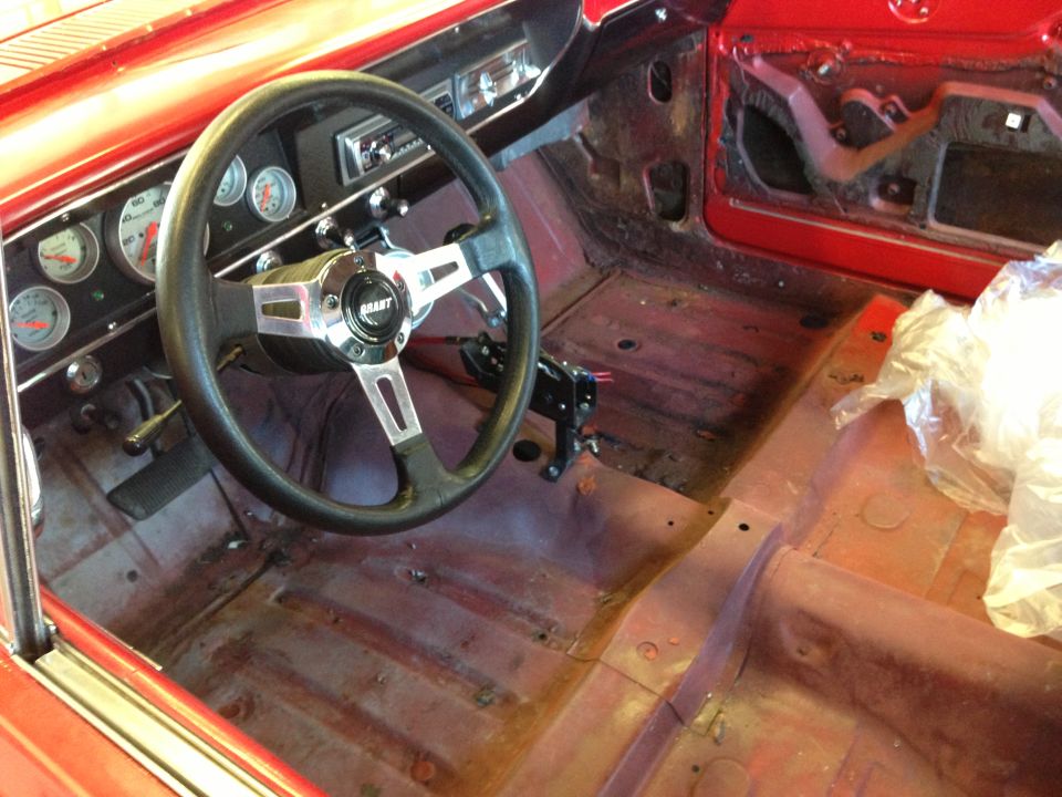 Red car interior with Grant steering wheel, aftermarket gauges, and bare floor panels