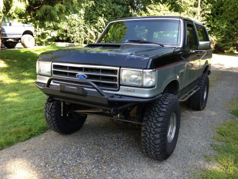 1989 Ford Bronco - A modified Ford Bronco sits on a gravel driveway, with another vehicle visible in the background.