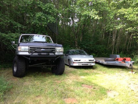 1989 Ford Bronco - This lifted Ford truck features a custom front bumper with a winch, parked in a grassy area with trees in the background.