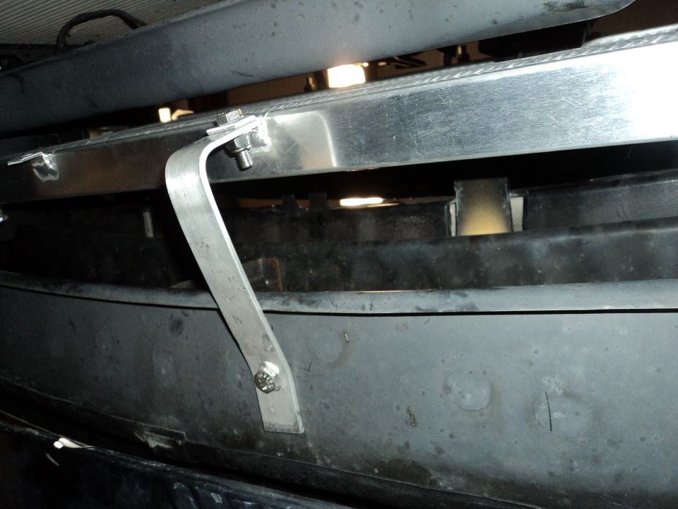 Close-up of an aluminum radiator bracket bolted to a dark plastic bumper