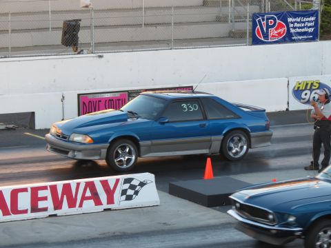 1990 Ford Mustang - A blue 1990 Ford Mustang is on the race track, with another car partially visible in the foreground.