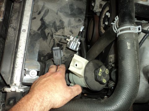 2004 Mercury Grand Marquis - Close-up view of the engine bay, focusing on the power steering reservoir and surrounding components. A hand is reaching towards the reserv…