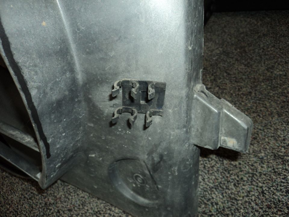 Close-up of a gray plastic automotive part with several black plastic clips attached