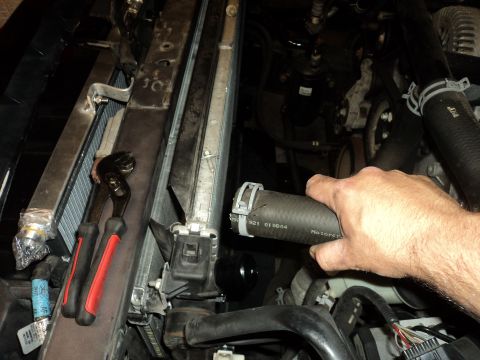 2004 Mercury Grand Marquis - Mechanic's hand holding a radiator hose in an engine bay, with tools nearby.