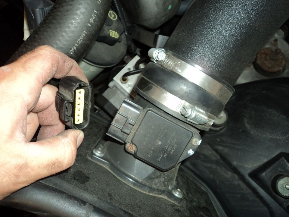 Hand holding connector to mass air flow sensor in engine bay