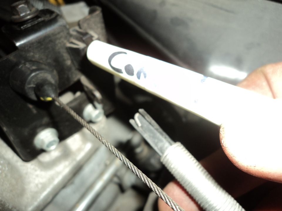 Close-up of a metal cable connected to an engine component, held by a hand with a white marker labeled 'Con'