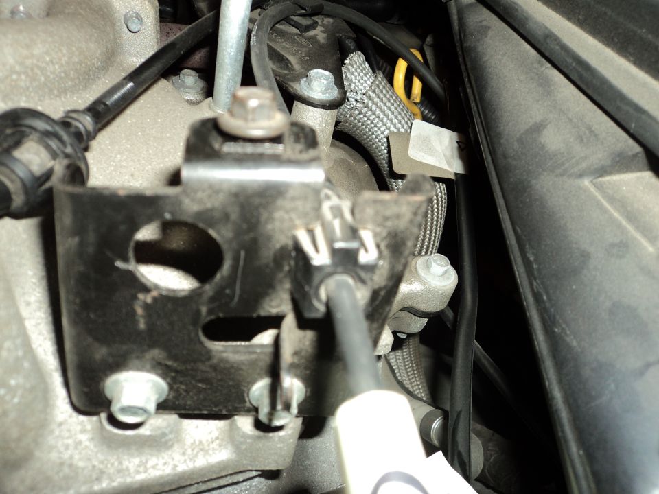 Close-up of a metal bracket attached to an engine component, with a cable and wiring harness visible