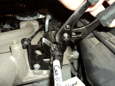 2004 Mercury Grand Marquis - A person uses pliers to work on a cable connection in the engine bay of a vehicle.