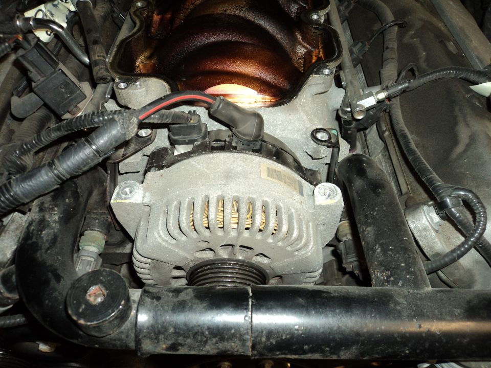 Close-up of a car's alternator and intake manifold with wiring harnesses