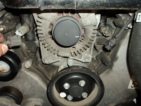 2004 Mercury Grand Marquis - Detail shot of an engine's alternator and associated components, with a hand interacting with a connector.