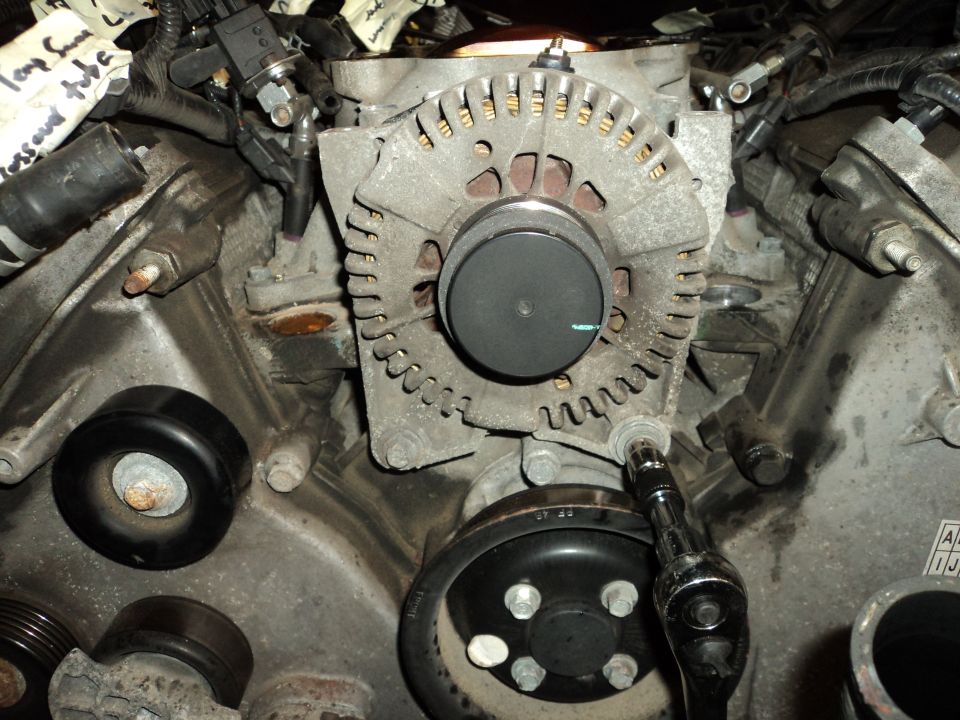 Alternator being worked on with a socket wrench, close-up engine view
