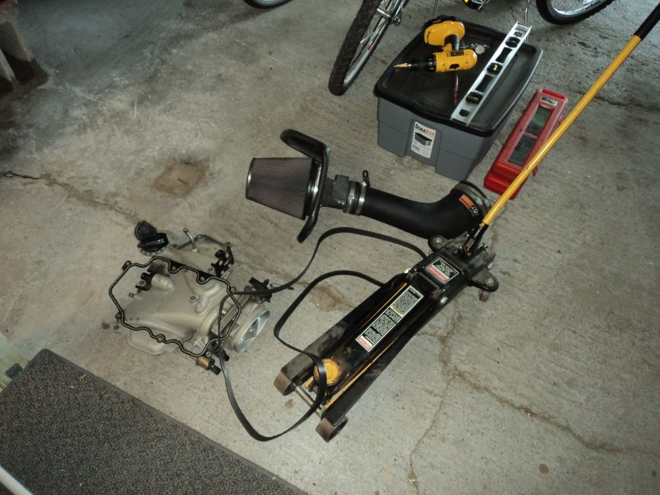 engine intake manifold, air filter, and a floor jack on a concrete floor