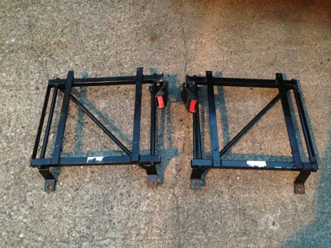 2004 Ford Crown Victoria - Two black metal seat frames with red seatbelt buckles are shown on a concrete surface.