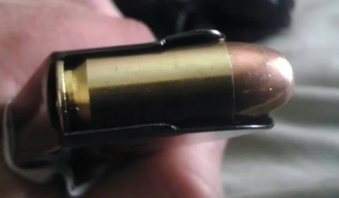 2000 Mercury Grand Marquis - A hand holds a magazine clip loaded with a single bullet, with the brass casing and copper projectile clearly visible.