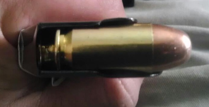 Close-up of a brass cartridge with a copper bullet in a black magazine, held by fingers