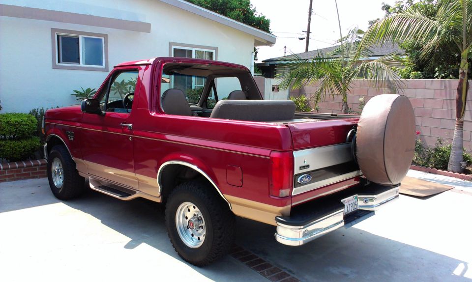 1994 Ford Bronco, red with tan lower body trim, removable top, and spare tire mounted on rear