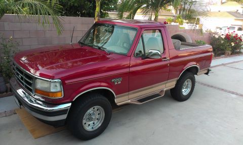 1994 Ford Bronco - This red Ford Bronco features tan trim, side steps, and a spare tire mounted in the cargo area.