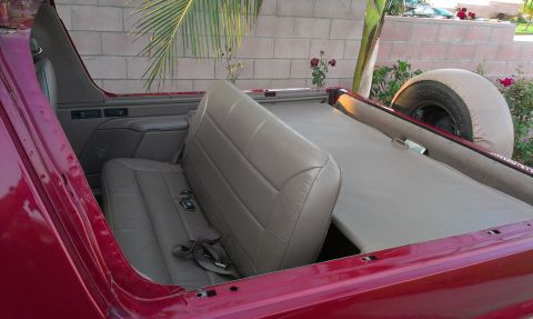 1994 Ford Bronco - The interior of a red Ford Bronco shows the rear seats and a spare tire mounted externally.