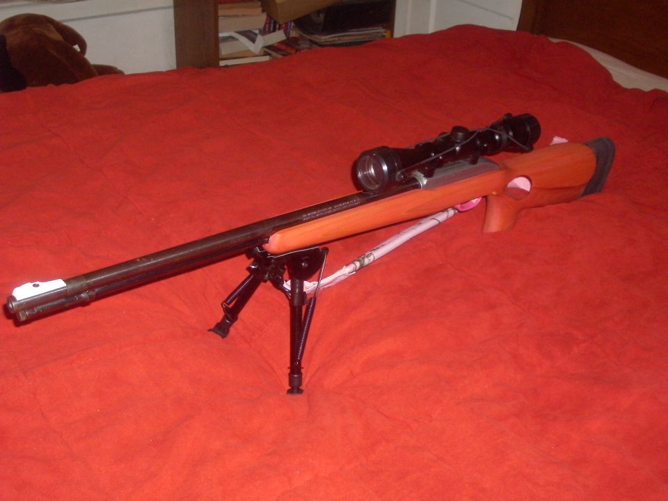 Rifle with scope and bipod on a red surface