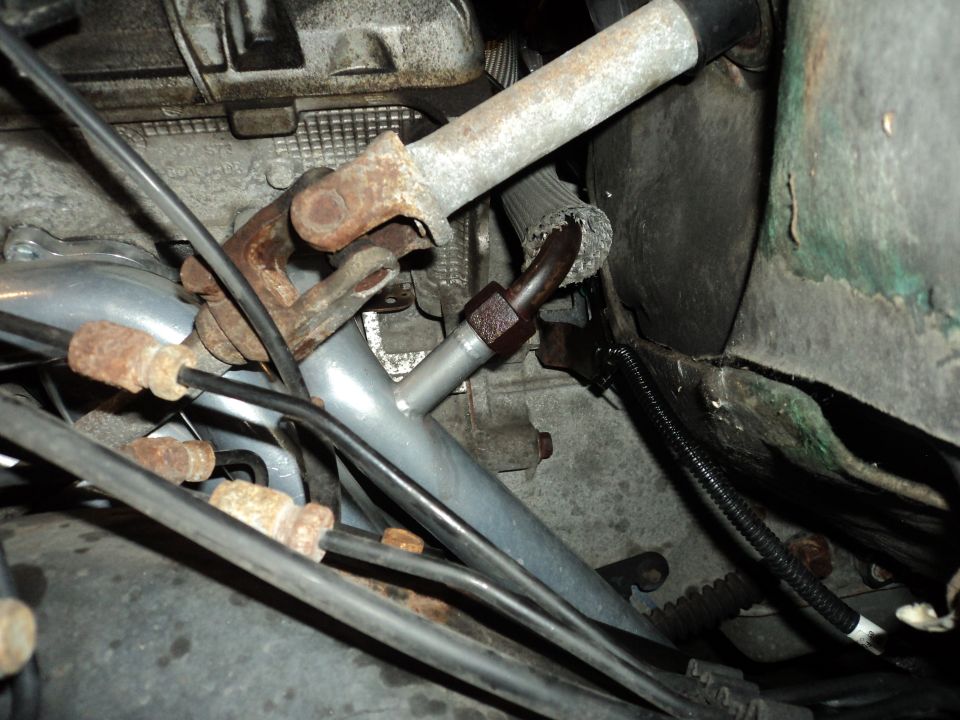 Close-up of steering linkage and engine components with various hoses and wires