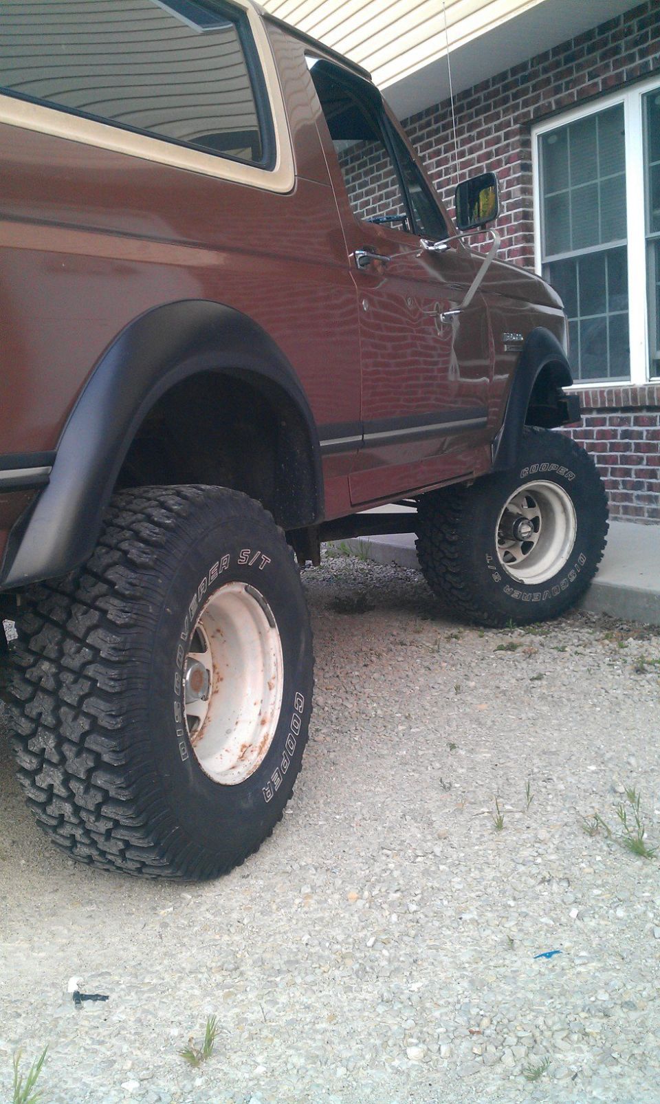 Brown 1987 Ford Bronco with lifted suspension and large tires parked next to a brick building