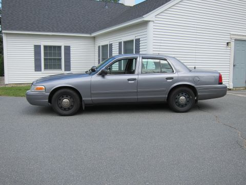 2001 Ford Crown Victoria - A gray 2001 Ford Crown Victoria sedan is parked in front of a white building.