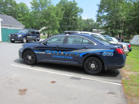 2001 Ford Crown Victoria - A blue police car with emergency lights is parked in a lot next to another police SUV and a white car.