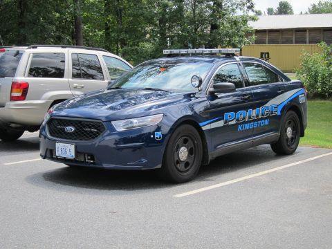 2001 Ford Crown Victoria - A dark blue police car with emergency lights on the roof is parked in a lot next to a silver SUV.