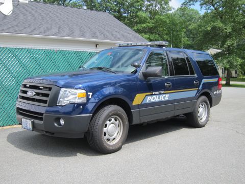 2001 Ford Crown Victoria - A blue police SUV is parked in front of a building with a green fence.