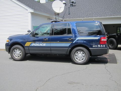 2001 Ford Crown Victoria - A blue police SUV is parked on asphalt in front of a building, with another dark vehicle visible to the right.